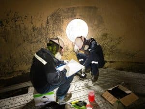 Inspectors documenting findings while working in confined spaces within a large, enclosed industrial tank.