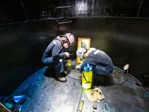 Two workers wearing protective gear working in confined spaces for industrial inspection and maintenance.
