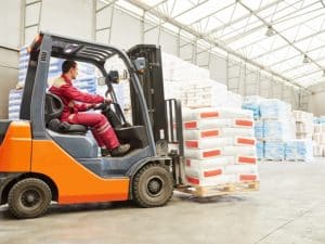Forklift operator transporting pallet in warehouse, highlighting forklift safety protocols for secure load handling.