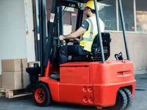 Warehouse worker on red forklift, wearing high-visibility gear to emphasize forklift safety practices.