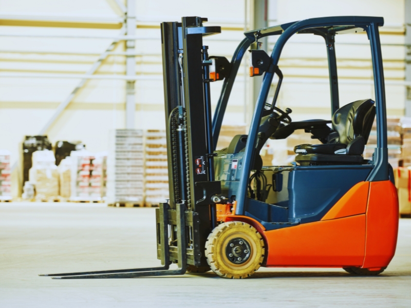 Modern warehouse forklift used for training on different types of forklift licences, parked indoors with stacked pallets nearby.