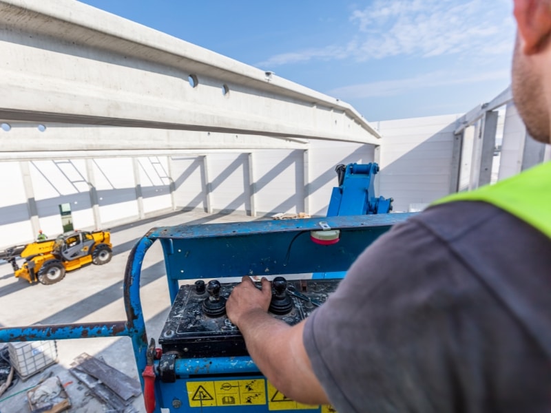 EWP operators manoeuvre a boom lift on a construction site with a telehandler visible in the background.